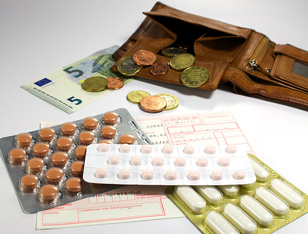 Mehrere verschiedene Tabletten und dahinter liegt eine fast leere Geldbörse