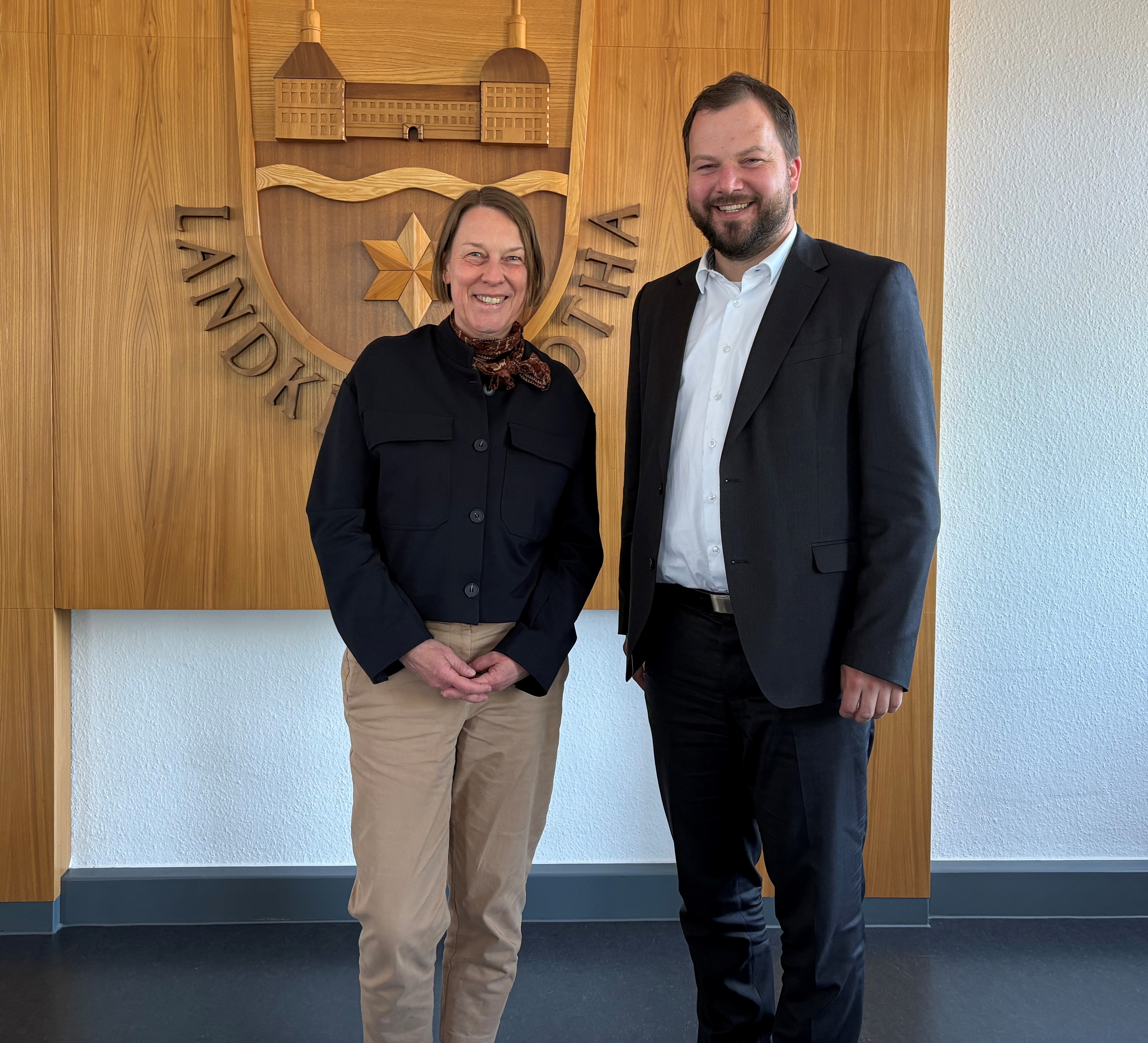 Democh und Eckert stehen nebeneinander vor Holzwand mit Emblem des Landkreises