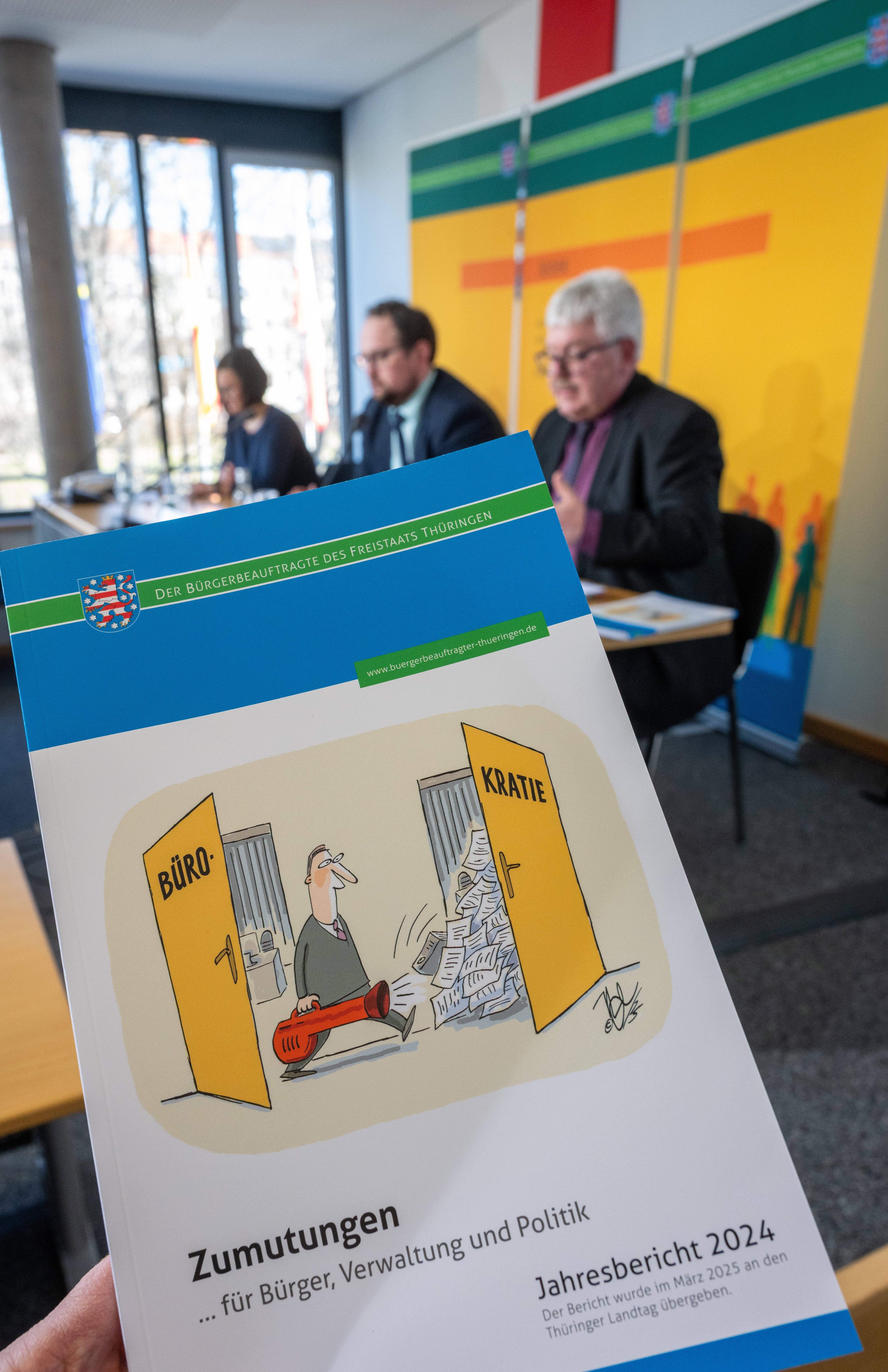 Der Bericht wird vor dem Podium in die Kamera hochgehalten